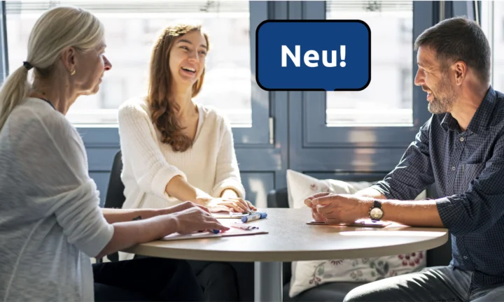 An einem runden Tisch sitzen drei Personen, zwei Frauen und ein Mann. Es wirkt, als ob sie miteinander sprechen, eine Frau lacht.