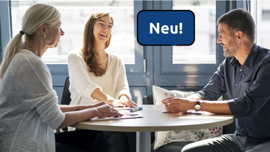 An einem runden Tisch sitzen drei Personen, zwei Frauen und ein Mann. Es wirkt, als ob sie miteinander sprechen, eine Frau lacht.